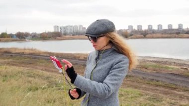 Blog yazarı kız telefonundan ve dalgalarından canlı yayın yapıyor. Açık havada ceketli bir kadın kameralı telefonla konuşuyor, kulaklıklar yayınlanıyor ve gülümsüyor. Teknoloji ve yaşam tarzı kavramı