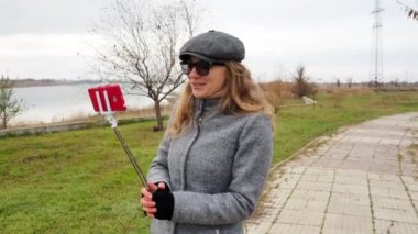 Park 'taki kız blogcu telefonda canlı yayında hoşça kal diyor, öpücükler yolluyor. Sonbahar montu giymiş açık havada konuşan ve gülümseyen bir kadın. Teknoloji ve yaşam tarzı kavramı