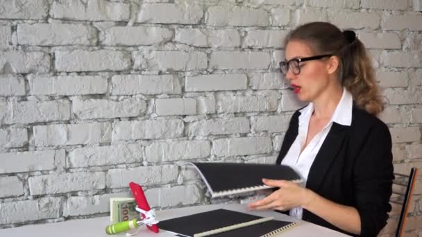 Chica blogger enseña negocios en una transmisión en línea en vivo a través de su teléfono inteligente. Mujer en un traje de negocios y gafas hojas a través de una carpeta de documentos y dirige una conferencia sobre ganar dinero. Copiar espacio — Vídeos de Stock