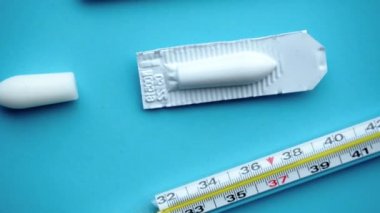 Mavi bir masada anal ya da vajinal kullanım için beyaz fitiller ve 38 derece sıcaklıkta termometre. Candida tedavisi için tıbbi mumlar, ardıç kuşu, hemoroit, iltihap ve ateş