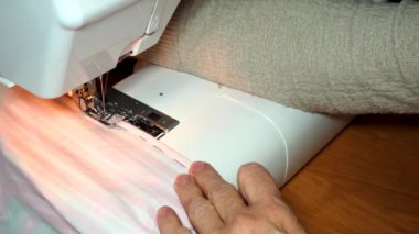 Yetişkin kadın terzi dikiş makinesine renkli kumaştan dikiş dikiyor. Eller yukarı. Kadın yanlış tarafa düz bir makine dikişi yapıyor. Elbise dikmek ve çarşaf dikmek evde ya da giysi fabrikasında