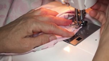 Yetişkin kadın terzi dikiş makinesine renkli kumaştan dikiş dikiyor. Eller yukarı. Kadın yanlış tarafa düz bir makine dikişi yapıyor. Elbise dikmek ve çarşaf dikmek evde ya da giysi fabrikasında