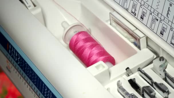 Eine rosafarbene Garnspule, die sich in einer Nähmaschine in Großaufnahme dreht. Eine Näherin macht einen glatten Maschinenstich. Herstellung von Kleidung und Bettwäsche zu Hause oder in einer Bekleidungsfabrik — Stockvideo