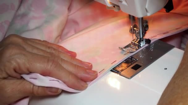 Adult woman seamstress sews from colored fabric on sewing machine.Hands close up. Woman makes a smooth machine stitch on wrong side. Making clothes and sewing bed linen at home or in a garment factory — Stock Video