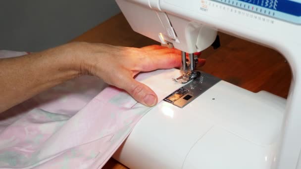 Adult woman seamstress sews from colored fabric on sewing machine.Hands close up. Woman makes a smooth machine stitch on wrong side. Making clothes and sewing bed linen at home or in a garment factory — Stock Video