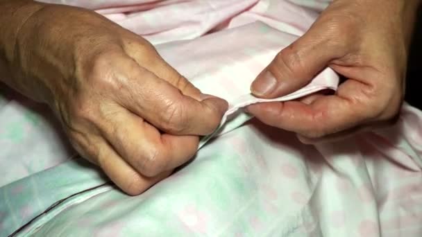 An adult woman seamstress sews impales the fabric with a needle. Hands close up. grandma makes a smooth hand stitch. Making clothes and sewing colored bed linen at home or in a garment factory — Stock Video