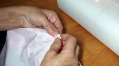 Yetişkin bir kadın terzi kumaşa iğne batırır. Eller yukarı. Büyükannenin el dikişleri pürüzsüz. Evde ya da giysi fabrikasında renkli çarşaf dikmek ve giysi dikmek.