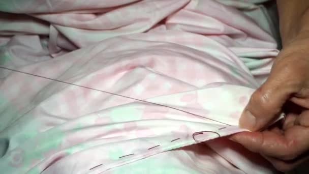 An adult woman seamstress sews impales the fabric with a needle. Hands close up. grandma makes a smooth hand stitch. Making clothes and sewing colored bed linen at home or in a garment factory — Stock Video