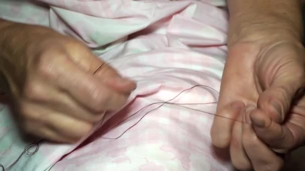 Vuxen kvinnlig sömmerska knyter en knut på en tråd. Händerna på nära håll. Kvinnan gör en jämn linje. Göra kläder och sy sänglinne hemma eller i en klädfabrik — Stockvideo