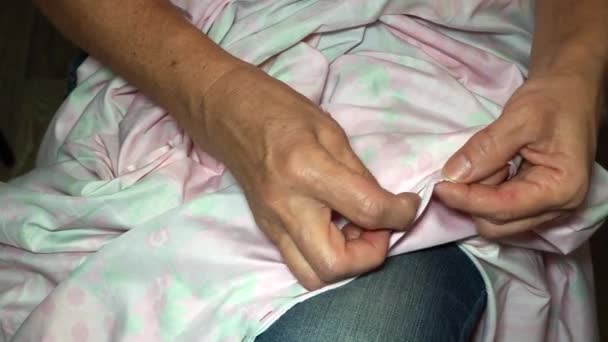 Eine erwachsene Näherin spießt den Stoff mit einer Nadel auf. Hände aus nächster Nähe. Oma macht einen geschmeidigen Handstich. Herstellung von Kleidung und Nähen farbiger Bettwäsche zu Hause oder in einer Bekleidungsfabrik — Stockvideo