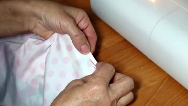 En vuxen kvinna sömmerska syr impales tyget med en nål. Händerna på nära håll. Mormor gör en smidig handstygn. Göra kläder och sy färgat sänglinne hemma eller i en klädfabrik — Stockvideo