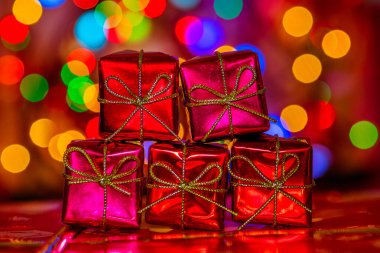 Renkli Bokeh çelenk ışıklarının arka planında beş tane kırmızı hediye kutusu. Tatil kartı. Altın kurdeleli ve fiyonklu hediyeler. Yeni yılın ışıltılı atmosferi.