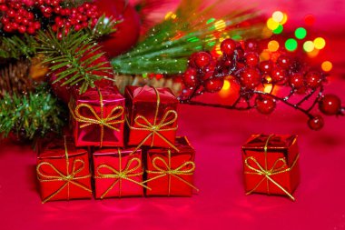 Kırmızı arka planda Noel hediyesi kutuları. Tatil kartı. Köknar dalları, böğürtlen, elma ve bokeh ışıklarının karışımı. Altın kurdeleli ve fiyonklu hediyeler. Yeni yılın atmosferi.