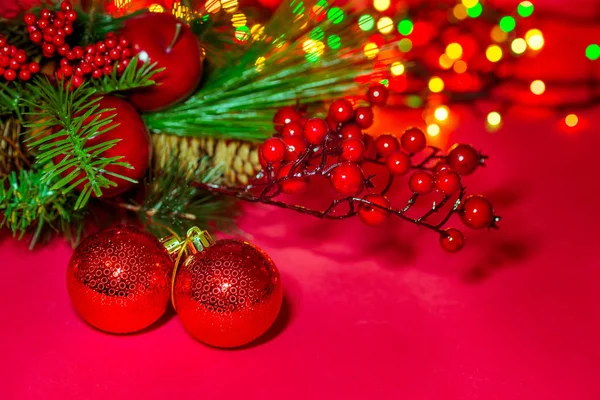 Dwie ozdobne kulki świąteczne na czerwonym tle. Świąteczna kartka. Skład choinki, jagód, jabłek i kolorowe światła bokeh girlandy. Klasyczna atmosfera nowego roku. Kopiowanie spazmy — Zdjęcie stockowe