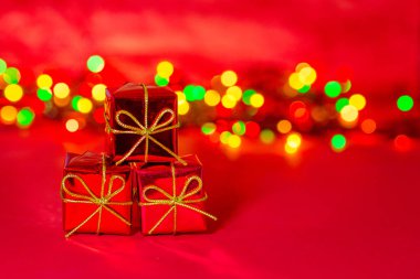 Noel 'de üç kırmızı hediye kutusu. Klasik renkli Bokeh çelenk ışıklarının arka planı. Tatil kartı. Altın kurdeleli ve fiyonklu hediyeler. Yeni yılın pırıl pırıl atmosferi. Boşluğu kopyala