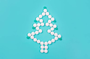 Mavi arka planda beyaz haplardan oluşan zarif bir Noel ağacı. Noel ve Yeni Yıl konsepti. Sağlık, tıbbi ve eczane zinciri tatili. Yaratıcı minimalist ilaçlar. Boşluğu kopyala