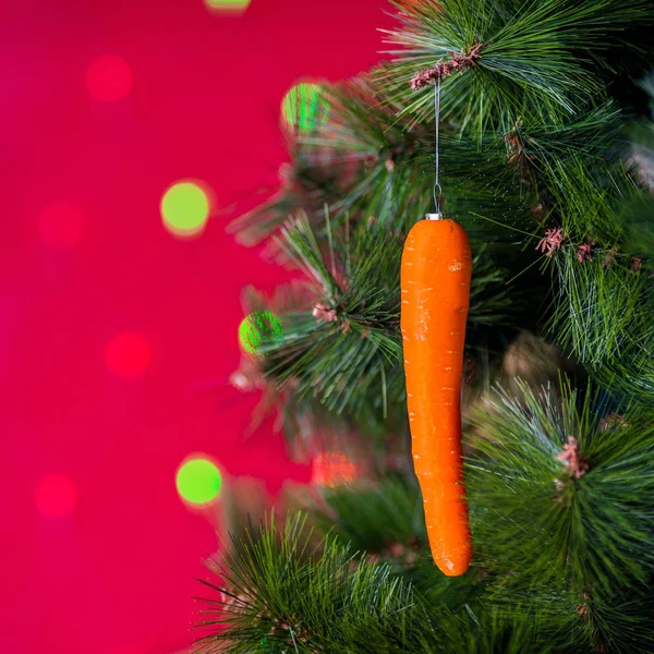 Wegański koncert świąteczny. Drzewo zdobią świeże warzywa. surowe marchewki na gałęzi sosny na czerwonym tle z bokeh. idea minimalizmu i ekologicznego świętowania bez marnotrawstwa. Przestrzeń kopiowania — Zdjęcie stockowe