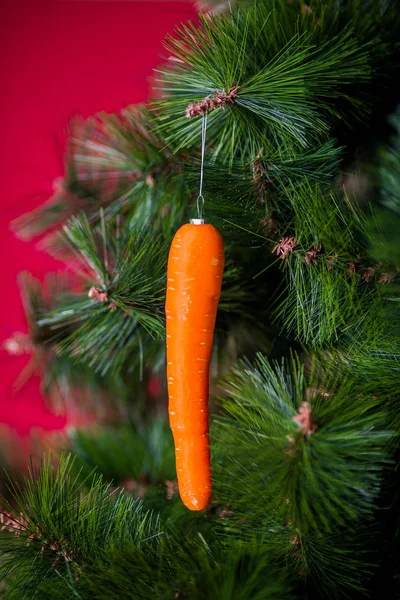 Wegański koncert świąteczny. drzewo ozdobione jest świeżymi warzywami. surowe marchewki na gałęzi sosny na czerwonym tle. Idea minimalizmu i ekologicznego świętowania bez marnotrawstwa. Przestrzeń kopiowania — Zdjęcie stockowe