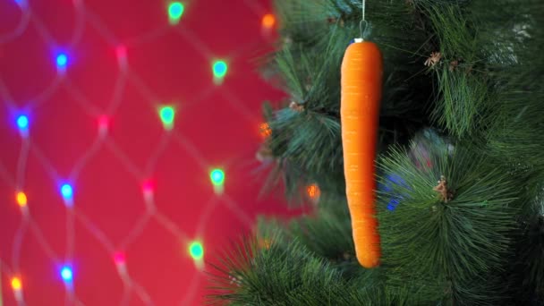 Vejetaryen Noel konseri. Ağaç taze sebzelerle süslenir. Kırmızı arka planda, çam dalında çiğ havuç ve bokeh. Minimalizm ve çevre dostu ziyan olmadan kutlama fikri. Boşluğu kopyala — Stok video