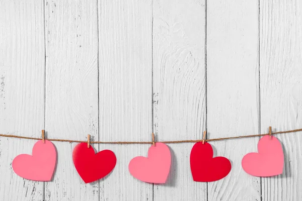 Wit geschilderde houten achtergrond met een slinger van rode en roze harten. Natuurlijk touw en wasknijpers. Concept van erkenning van liefde, romantische relaties, Valentijnsdag in grunge stijl. Kopieerruimte — Stockfoto