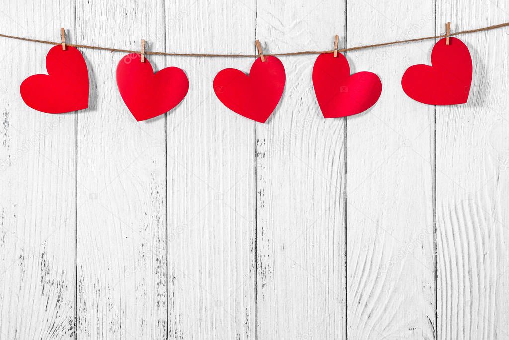 White painted wooden background with a garland of red hearts. Natural rope and clothespins. Concept of recognition of love, romantic relationships, Valentines day in grunge style. Copy space