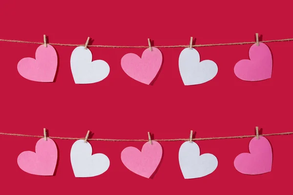 Garland of pink and white hearts on a red classic background. Natural rope and clothespins. Concept of Declaration of love, wedding, romantic relationship, Valentines Day. Copy space — 스톡 사진