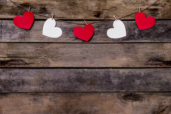 Oude houten achtergrond met een slinger van rode en witte harten. Natuurlijk touw en wasknijpers. Concept van erkenning van liefde, romantische relaties, Valentijnsdag in grunge stijl. Kopieerruimte — Stockfoto