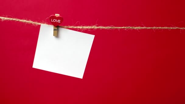 Un trozo de papel blanco sobre cuerda con un tendedero, con espacio para el texto. Notas burlonas sobre un fondo clásico rojo. Concepto de reconocimiento de amor, boda, relación romántica, día de San Valentín — Vídeo de stock