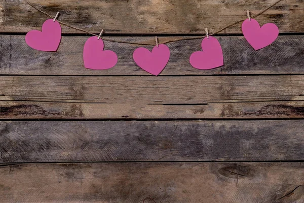 Old wooden background with a garland of pink hearts. Natural rope and clothespins. Concept of recognition of love, romantic relationships, Valentines day in grunge style. Copy space — 스톡 사진
