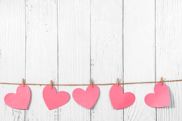 Wit geschilderde houten achtergrond met een slinger van roze harten. Natuurlijk touw en wasknijpers. Concept van erkenning van liefde, romantische relaties, Valentijnsdag in grunge stijl. Kopieerruimte — Stockfoto