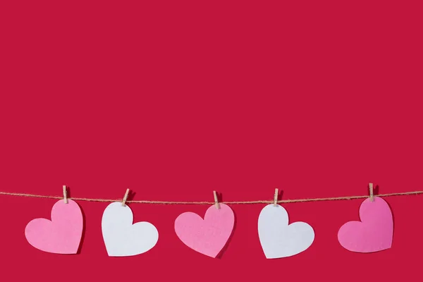 Garland of pink and white hearts on a red classic background. Natural rope and clothespins. Concept of Declaration of love, wedding, romantic relationship, Valentines Day. Copy space — 스톡 사진