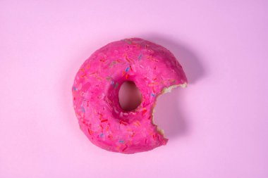 İzole bir arka planda yarısı yenmiş pembe bir çörek. Parlak lezzetli çörek. Tatlı yiyeceklerden arta kalanlar. Minimum yaz konsepti. Uzayı kopyala Düz yatıyordu. Sağlıklı bir diyet ve kilo alma değil..