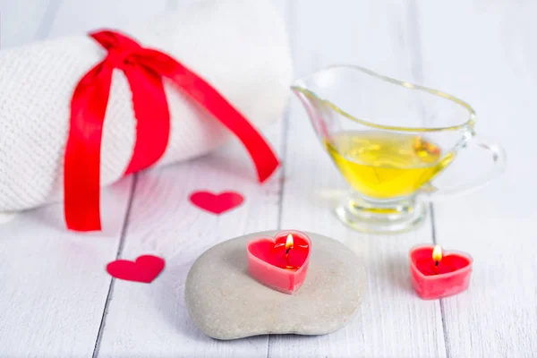 O conceito de um Spa no Dia dos Namorados. Velas em forma de coração vermelho, pedras, óleo de massagem e uma toalha branca em um fundo de madeira. Relaxamento e bem-estar. Procedimento de banho . — Fotografia de Stock