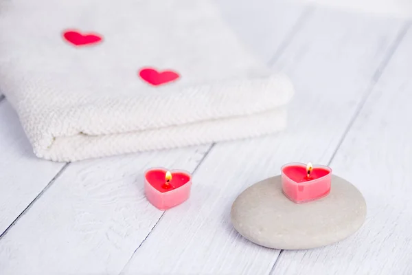 Koncept lázní na Valentýna. Červené svíčky ve tvaru srdce, kameny a bílý ručník na dřevěném pozadí. Relaxační a wellness péče. Koupací procedura. — Stock fotografie