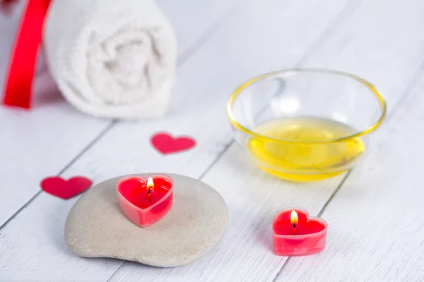 The concept of a Spa on Valentines Day. Red heart-shaped candles, stones, massage oil and a white towel on a wooden background. Relaxation and wellness care. Bath procedure.