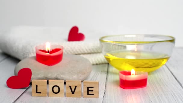 Koncepcja Spa w Walentynki. Spalić czerwone świece w kształcie serca, kamienie, olej do masażu, słowo miłość i biały ręcznik na drewnianym tle. Relaks i opieka wellness. Zabieg kąpielowy, kosmetologia — Wideo stockowe