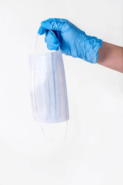 Personal protection against colds and viruses. A medical workers hand in blue gloves drops a protective mask on a white background. The concept of maintaining health during the flu season.Copy space