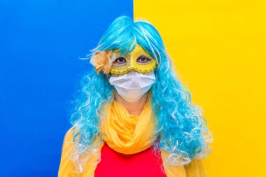 Karnavalda Coronavirus 'a karşı koruma kavramı. Mavi peruklu ve sarı karnaval maskeli, Virüs tacından bir sağlık maskesi takan ve bayramı neşeyle kutlayan zeki bir kadın..