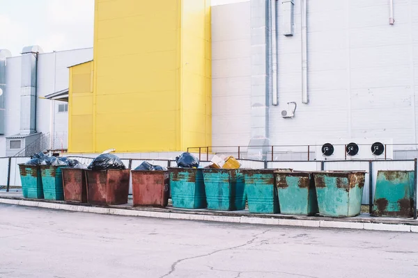 Recipientes de lixo transbordantes com lixo perto de um edifício industrial. Problema ambiental da eliminação de resíduos sólidos numa grande cidade. Conceito de poluição ambiental . — Fotografia de Stock