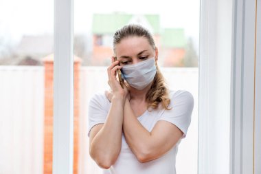 Ev karantinası. Sağlık koruma maskesi takmış beyaz bir kadın, telefon eder, ambulans çağırır. Kötü sağlık, yüksek sıcaklık, mevsimsel grip ve grip salgını. Ev tedavisi