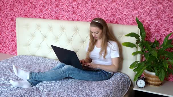 自宅でリモートワーク。ベッドの上の彼女の寝室でノートパソコンで働いている美しい白人の女の子。ビジネスとe教育の概念。ウイルスの流行中にオンラインで学ぶ学生. — ストック動画