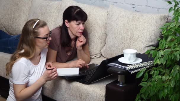 Travail à distance depuis la maison. Deux femmes travaillant ensemble sur un ordinateur portable sur le canapé du salon, discutant d'un projet. Formation en ligne anglais e-education. Volgodonsk, Russie-07 avril 2020 . — Video