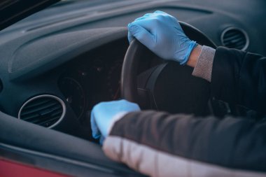 Bir adam koruyucu tıbbi eldivenlerle bir arabanın direksiyonunu tutuyor. Eller yakın çekim. Salgın koronavirüs sırasında takside güvenli sürüş. Sürücü ve yolcuları bakteri ve virüs enfeksiyonundan koru.