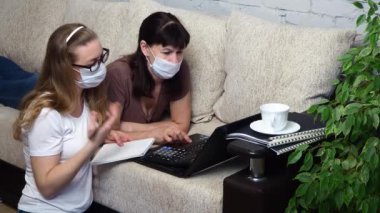 Evden uzak bir iş. Koruyucu tıbbi maskeli iki kadın oturma odasındaki kanepede dizüstü bilgisayarda birlikte çalışıyor ve projeyi tartışıyorlar. E-eğitim