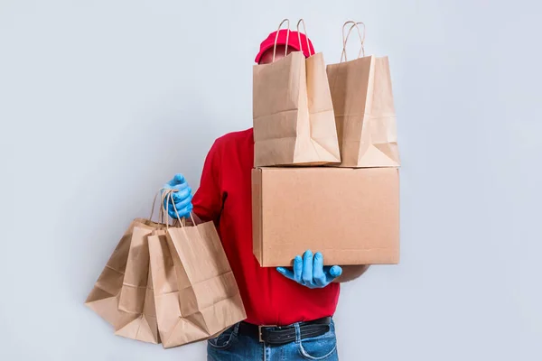 安全な配達の概念 赤い制服と保護マスクと手袋の宅配便は 大規模な注文 段ボール箱と多くの紙袋 検疫での注文の非接触配達を保持しています — ストック写真
