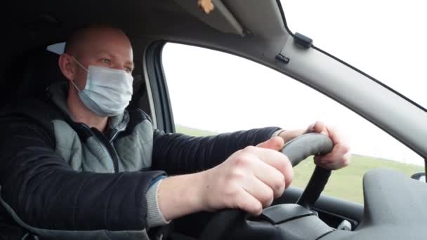 En man som kör bil i en skyddande mask. Säker körning i taxi under en pandemisk coronavirus. Skydda förare och passagerare från bakterier och virusinfektion i karantän. — Stockvideo