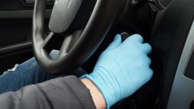 Kapatın. Koruyucu tıbbi eldivenlerle arabanın direksiyonundaki adamın elleri anahtarı kontağa takar ve sürmeye başlar. Koronavirüs salgınından korunmak için karantina sırasında güvenli taksi yolculuğu.