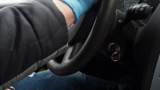 Närbild. Händerna på en man som kör bil i skyddshandskar stannar bilen och tar fram tändningsnyckeln. Säker taxiresa under karantänen från coronavirus pandemi. Ryssland, Volgodonsk 16 april 2020. — Stockvideo