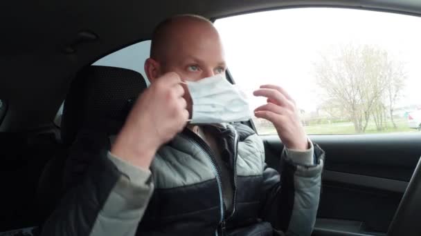 Een man in een auto draagt een beschermend medisch masker. Veilige taxirit tijdens de coronavirus pandemie. Bescherm de bestuurder en passagiers tegen bacteriële en virale infecties in quarantaine. — Stockvideo