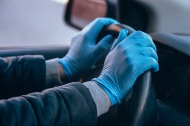 Bir adam koruyucu tıbbi eldivenlerle bir arabanın direksiyonunu tutuyor. Eller yakın çekim. Salgın koronavirüs sırasında takside güvenli sürüş. Sürücü ve yolcuları bakteri ve virüs enfeksiyonundan koru